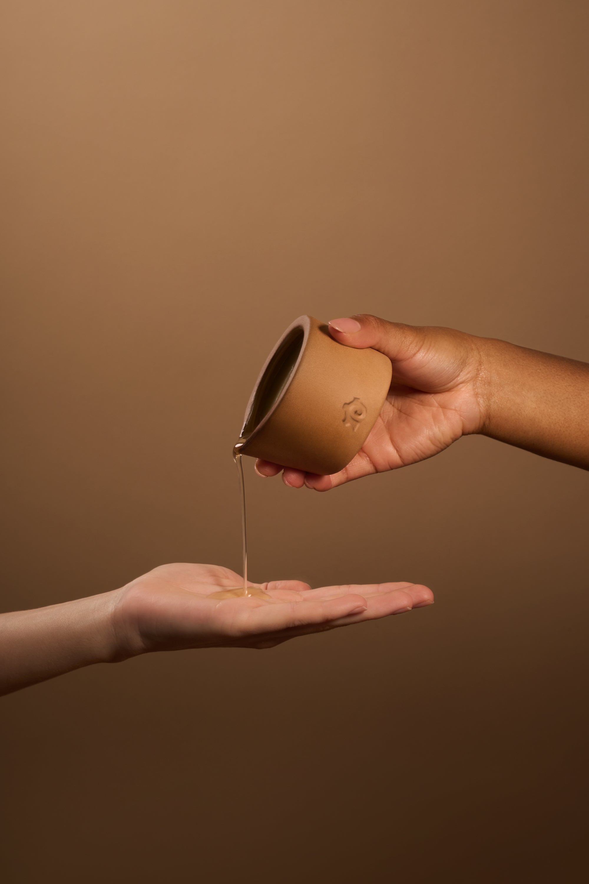 Person pouring serum from a small handmade vessel into another person's palm